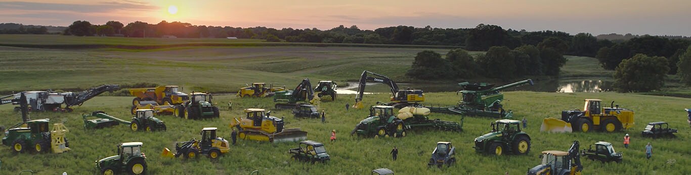 Várias pessoas a caminhar num campo de grandes dimensões, no meio de vários tipos de equipamentos da John Deere.