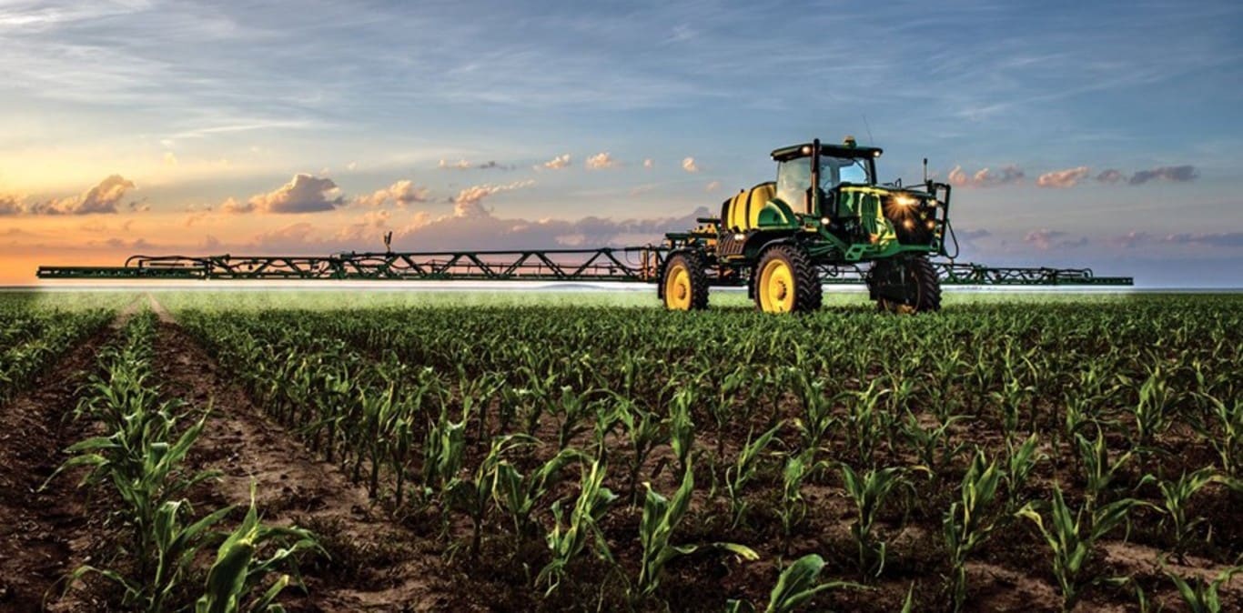 Pulverizador John Deere trabalhando num campo de milho ao pôr-do-sol