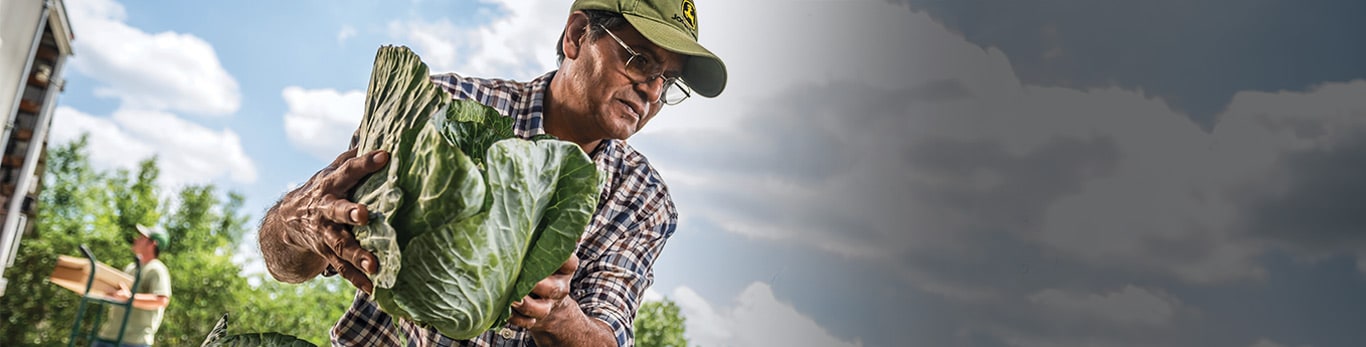 Um homem com um capacete de proteção num local de trabalho com equipamento John Deere nas proximidades