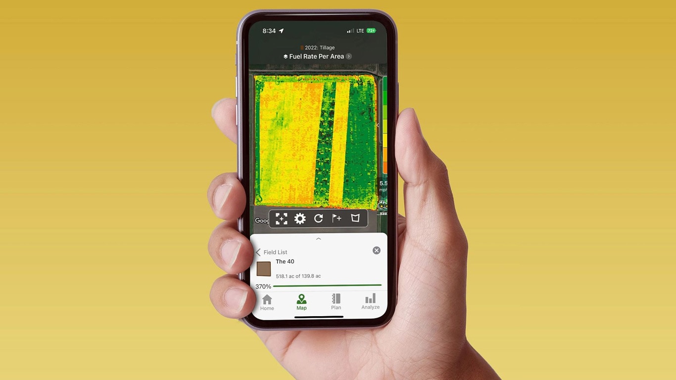 Mão a segurar um telemóvel inteligente que apresenta um Centro de Operações John Deere com dados sobre a taxa de combustível.