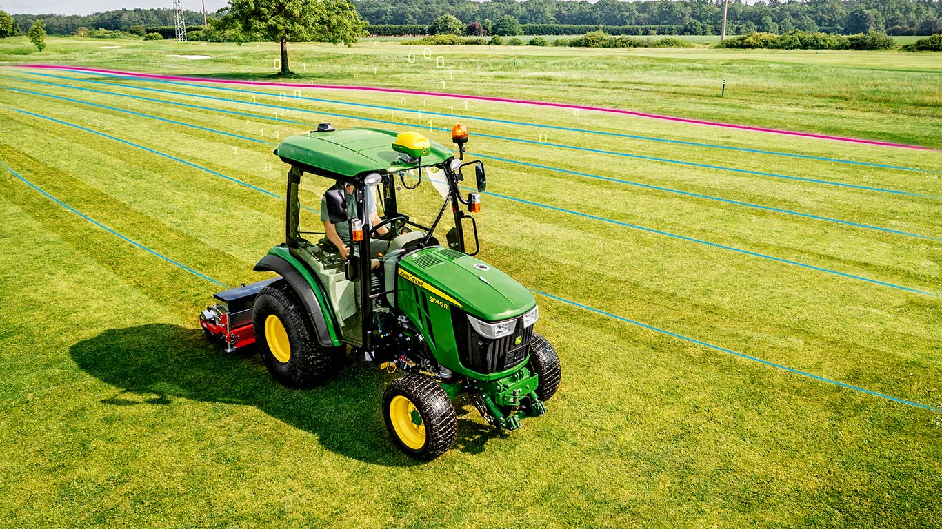 Um greenkeeper está a utilizar um trator utilitário compacto da John Deere numa área de relva.