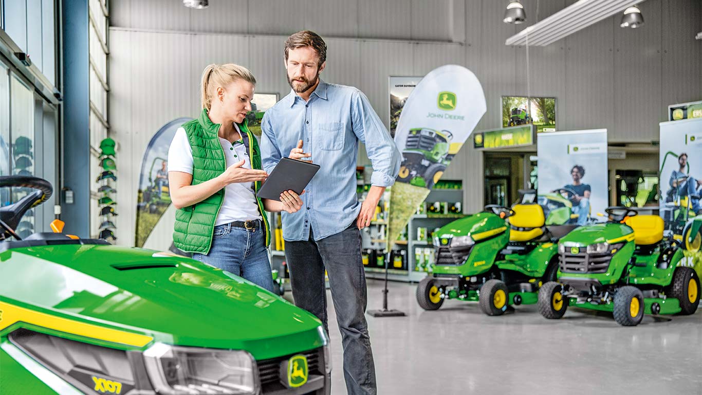 Um concessionário John Deere está a aconselhar um cliente relativamente à compra de um cortador de relva John Deere.