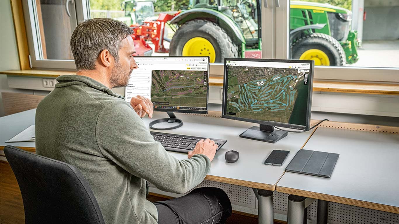 Um supervisor de greenkeepers está a olhar para os mapas de um campo de golfe no seu computador.