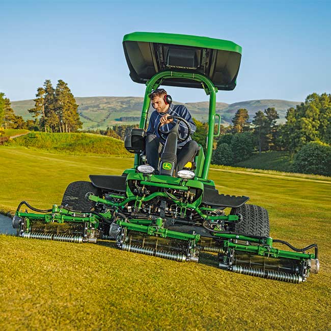 Um greenkeeper está a utilizar uma máquina tripleta de greens da John Deere numa área de relva (vista frontal).