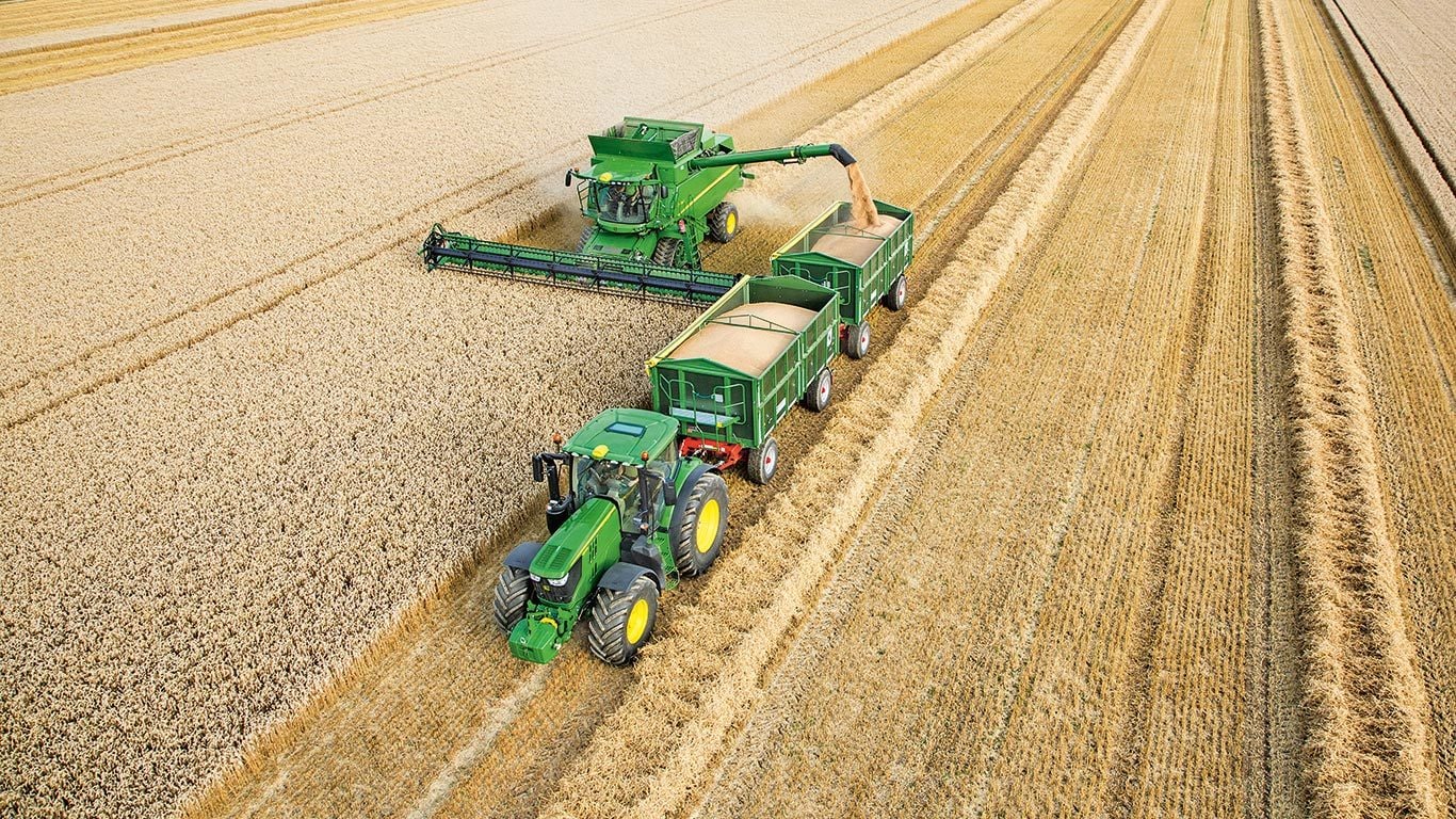 Ceifeira-debulhadora S&eacute;rie S John Deere a descarregar trigo para dois reboques puxados por trator