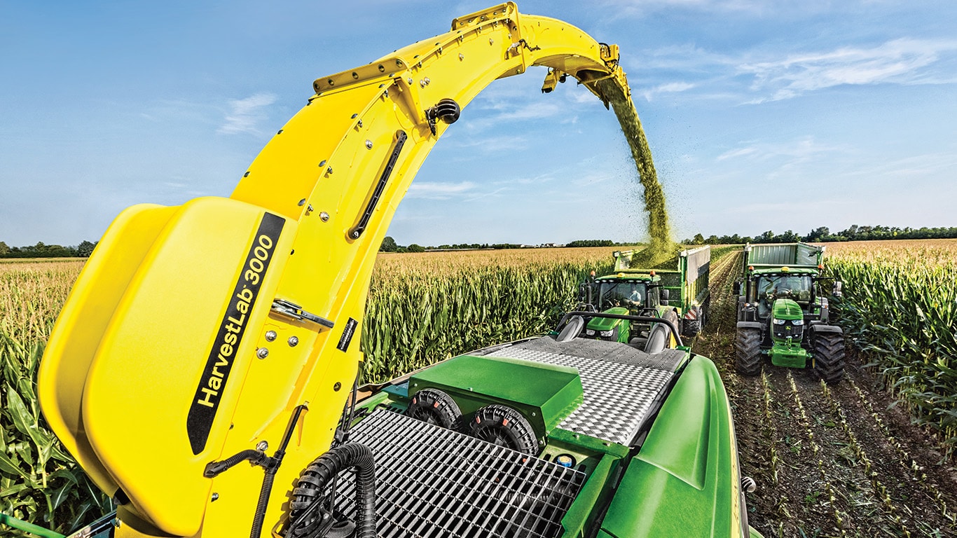 Vista da traseira da picadora de forragem automotriz John Deere S&eacute;rie 9000 com dois reboques de silagem puxados diretamente atr&aacute;s por tratores John Deere