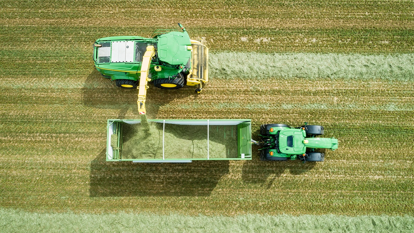 Foto a&eacute;rea da colhedoras automotriz John Deere S&eacute;rie 8000 com um recolhedor de forragem a carregar silagem para um reboque puxado por um trator John Deere