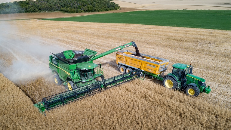 Ceifeira-debulhadora S&eacute;rie X John Deere a descarregar sementes de colza para um reboque de gr&atilde;os puxados por um trator John Deere